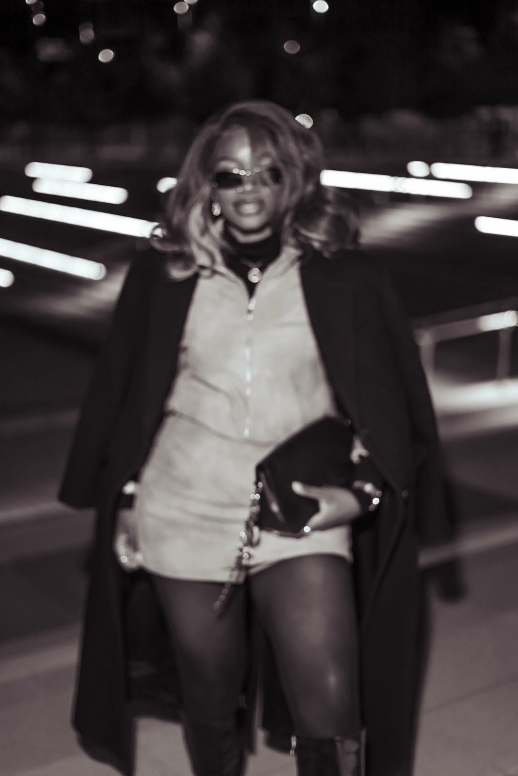 Personne souriante en manteau long marchant vers l'objectif, la nuit.