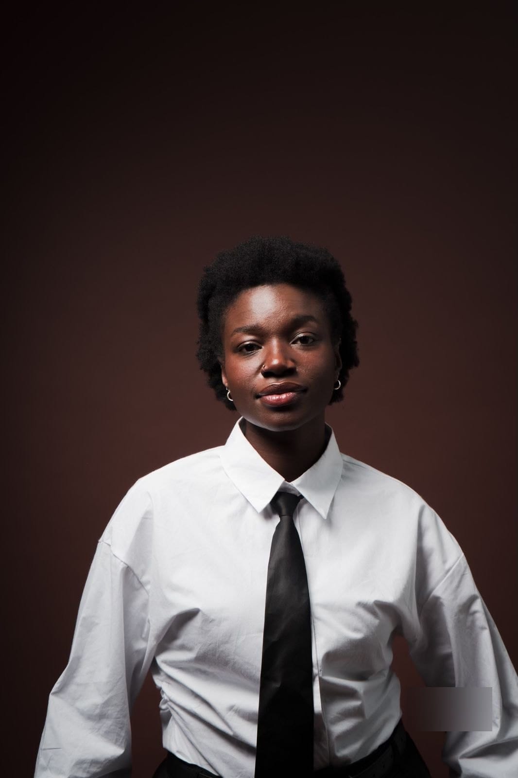 Portrait en studio, personne en chemise blanche et cravate noire, fond brun.