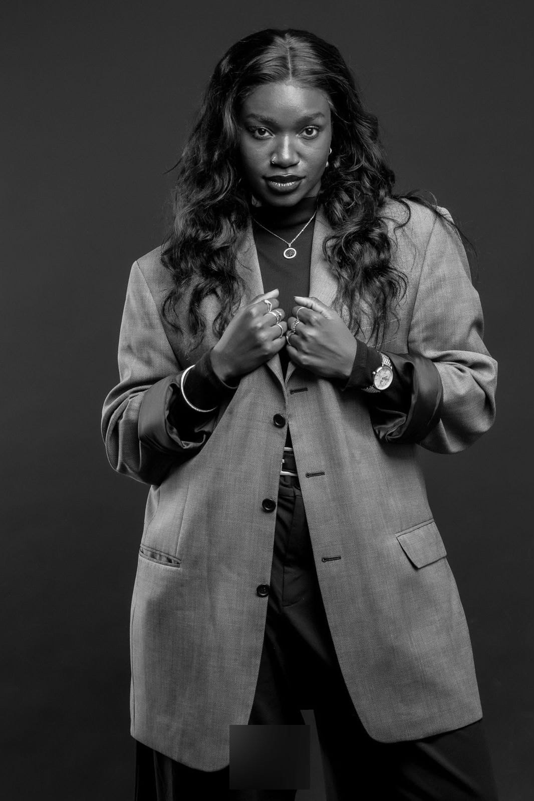Femme en veste oversize, mains sur le col, regard frontal.