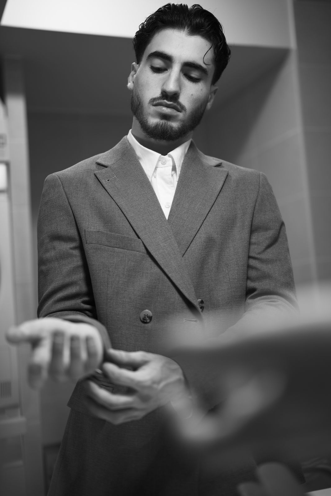 Homme en costume gris, les yeux baissés, mains occupées au poignet.
