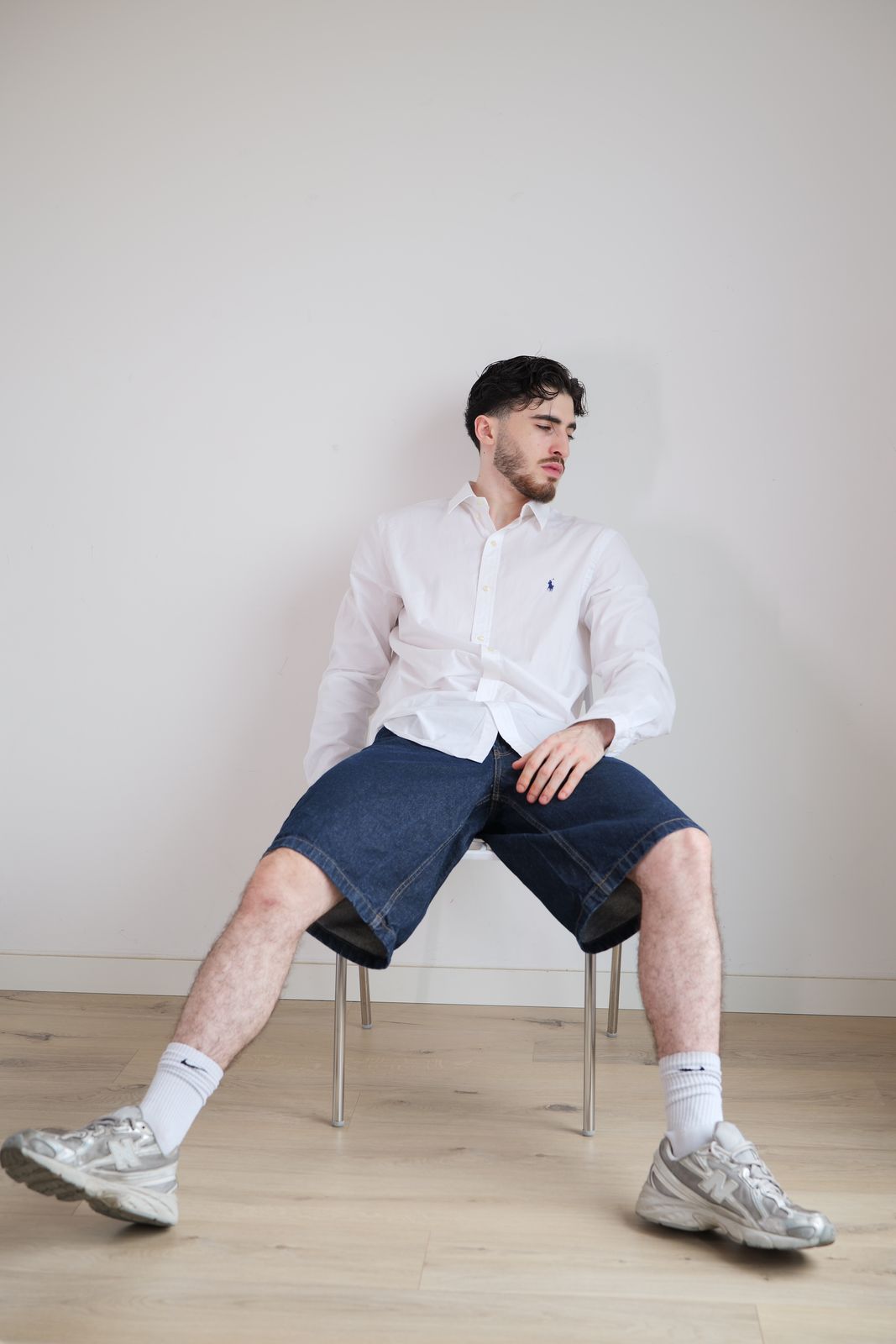 Homme assis sur une chaise, chemise blanche, devant un mur clair.