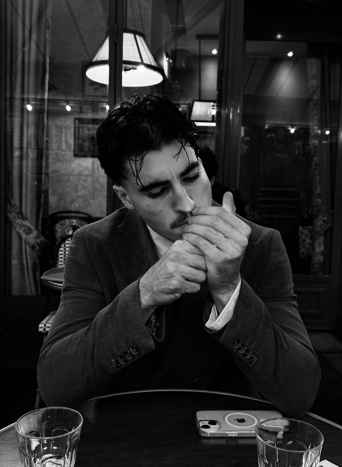Personne assise à une table, yeux clos, mains jointes près du visage.