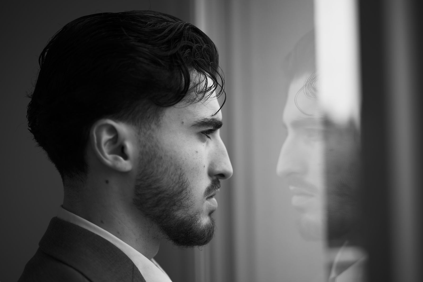 Profil d'un homme face à son reflet dans une vitre.