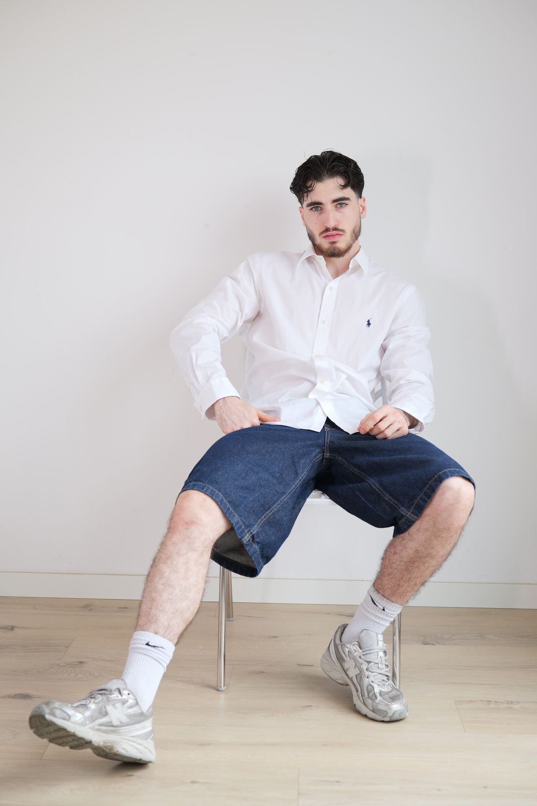 Homme assis, chemise blanche, bermuda en jean, regard face caméra.