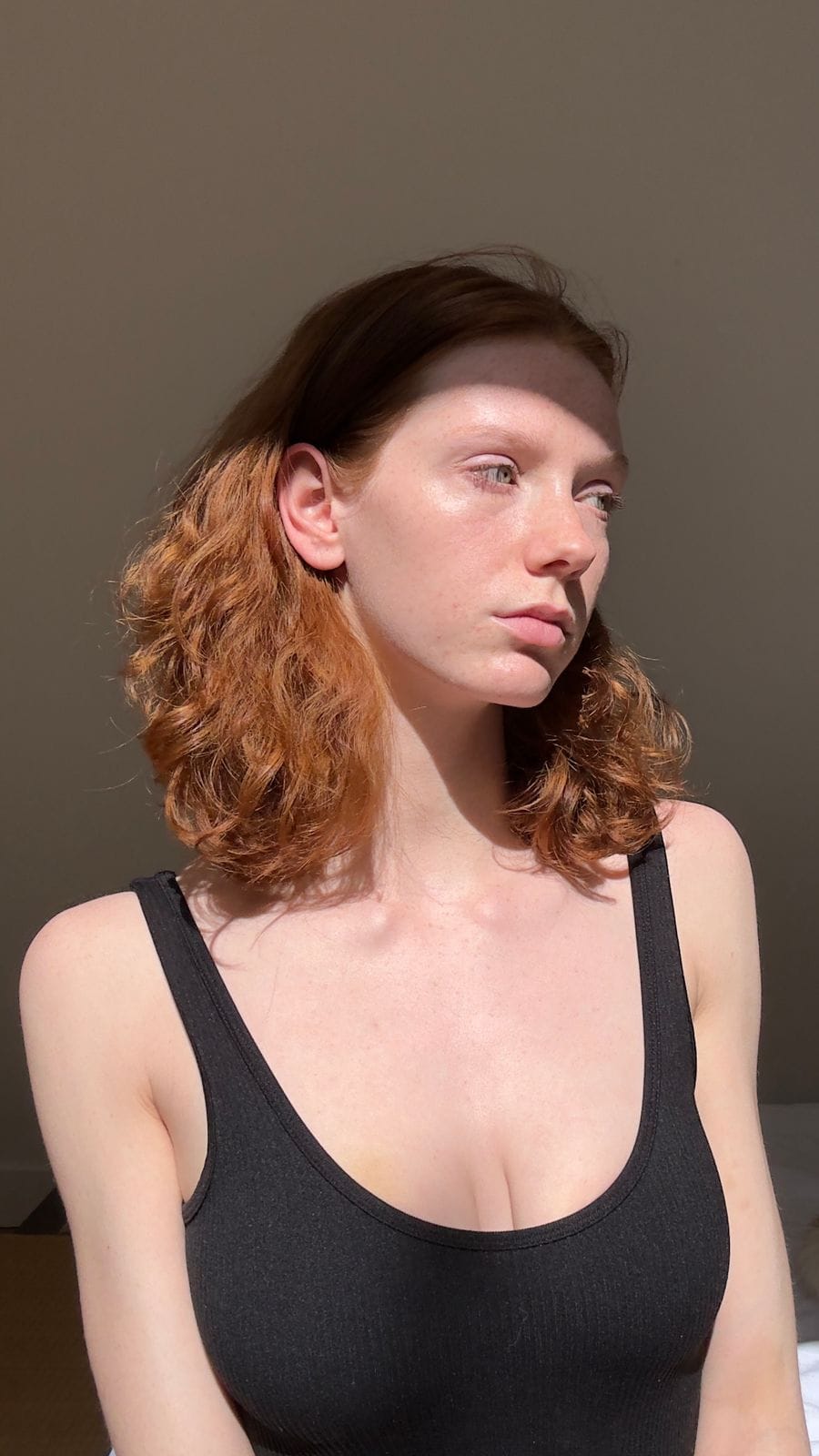 Personne rousse de trois quarts, éclairée par le soleil, débardeur noir.