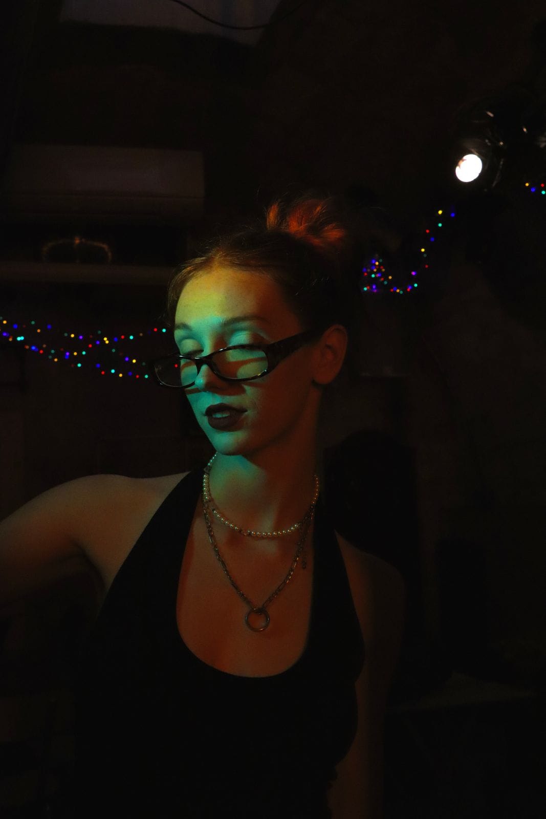 Personne à lunettes, chignon, lumière verte dans une pièce sombre.