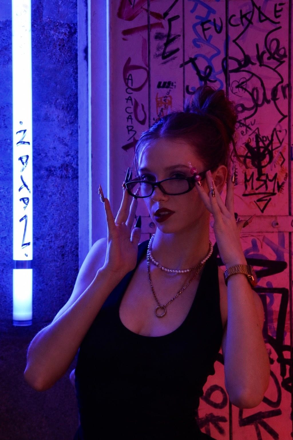 Personne aux lunettes, mains sur la monture, éclairage néon bleu et rose.
