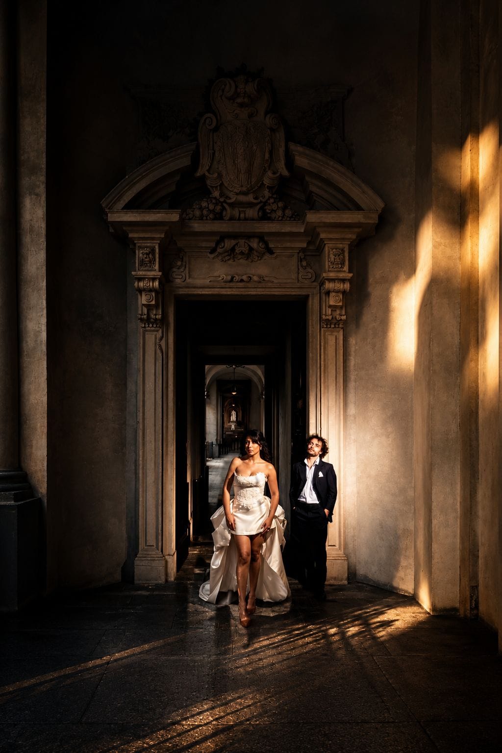 Couple en tenue habillée dans un encadrement ornementé, lumière latérale.
