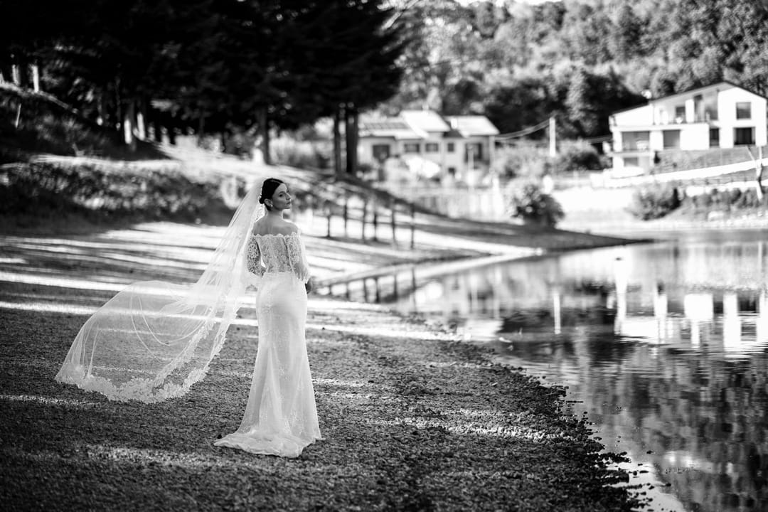 Femme en robe de mariée, voile au vent, bord de lac.