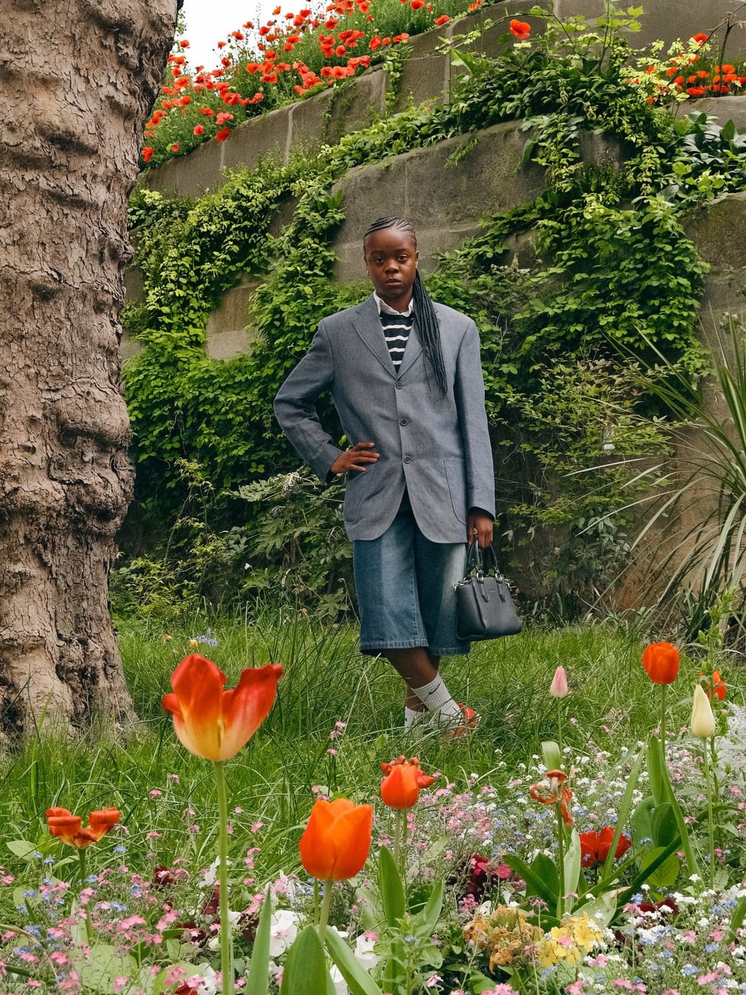 Personne debout dans un jardin fleuri, tulipes orange au premier plan.
