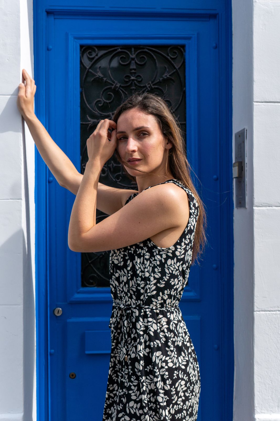 Femme en robe imprimée, main levée devant une porte bleue.